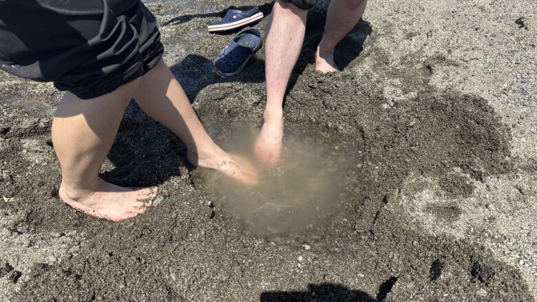 屈斜路湖砂湯で掘った湯だまりに足を入れる様子